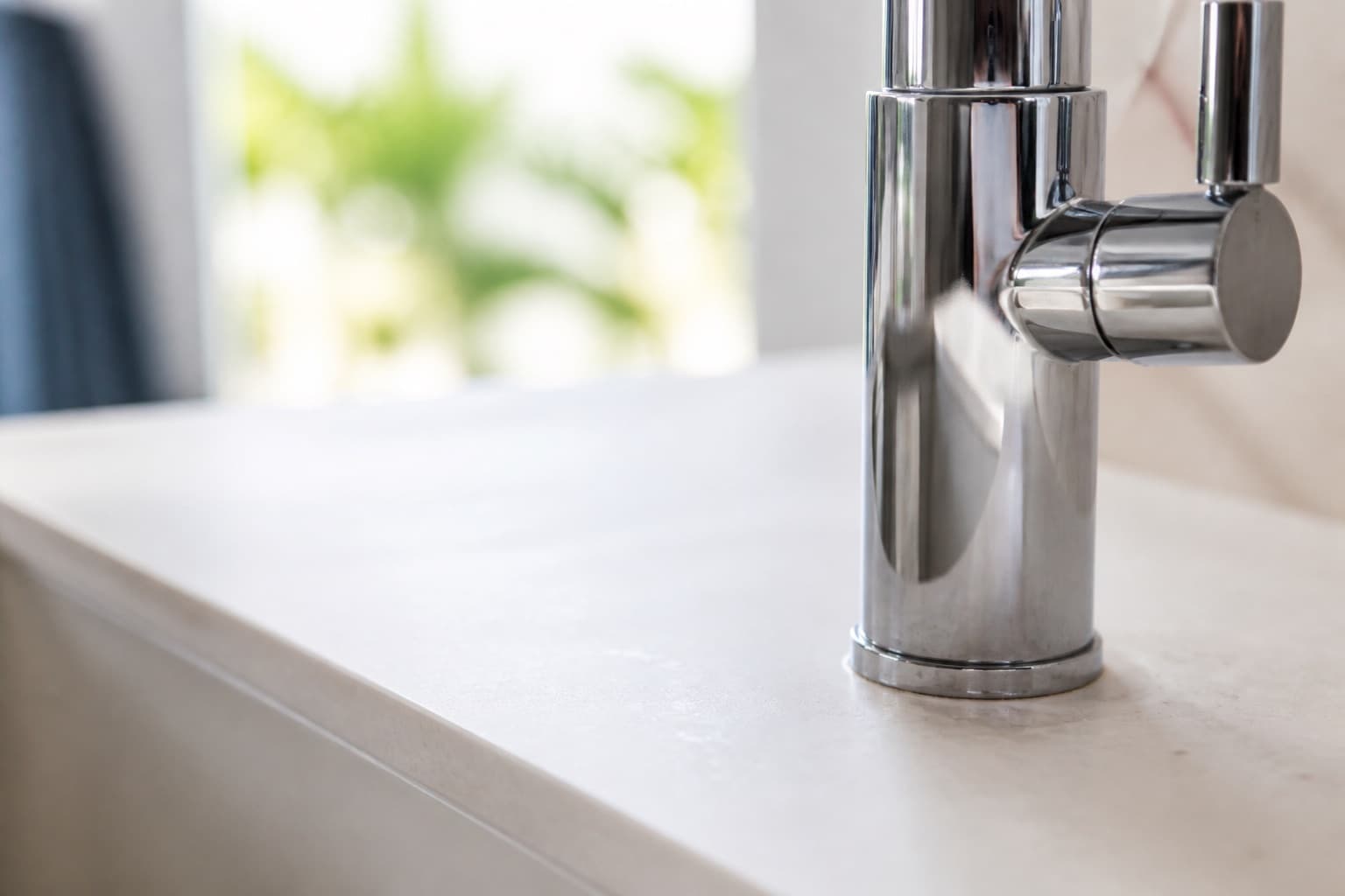 Chrome faucet with a light mineral ring and faint water spots on a pale stone surface